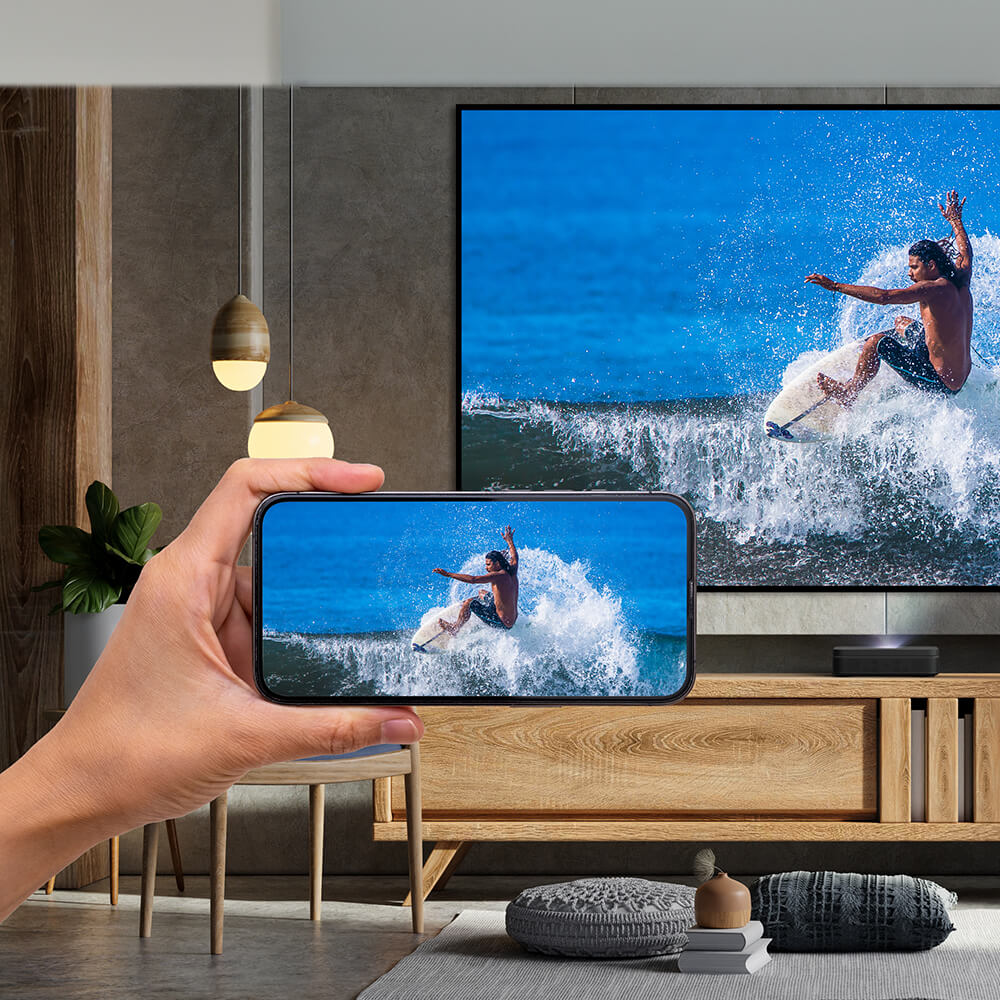Person streaming video from smartphone to large TV screen showing surfer riding wave, demonstrating wireless screen mirroring technology in modern living room